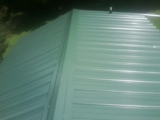 New green metal panels meeting at the ridge of a roof — Flat Roof Repair work by our crew in Grant